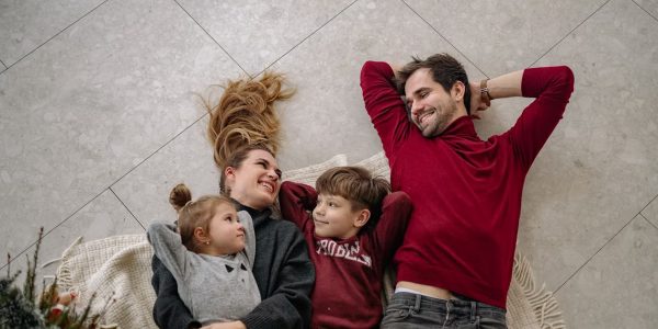 Smiling family of four lying on a blanket, sharing happiness and love indoors.