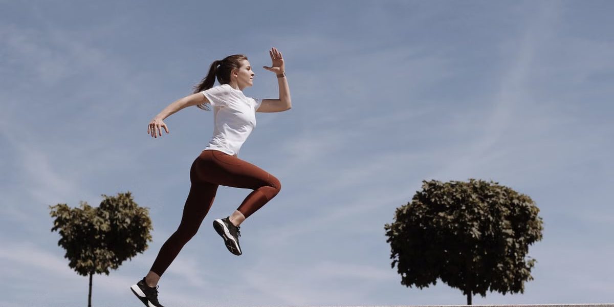 Athletic woman running on an outdoor road, demonstrating fitness and determination under a blue sky.