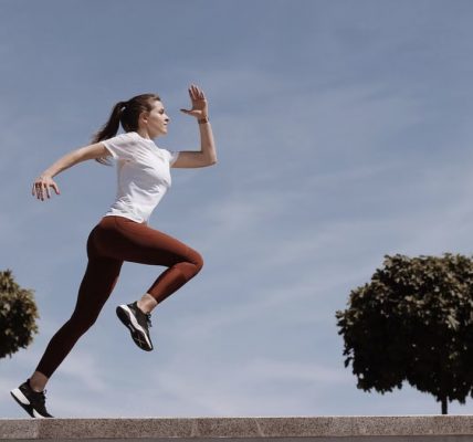 Athletic woman running on an outdoor road, demonstrating fitness and determination under a blue sky.